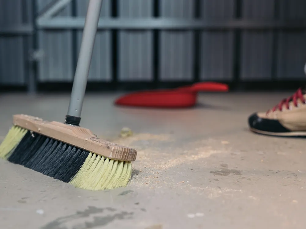 Cepillo de barrer retirando polvo y restos de obra sobre un suelo de hormigón