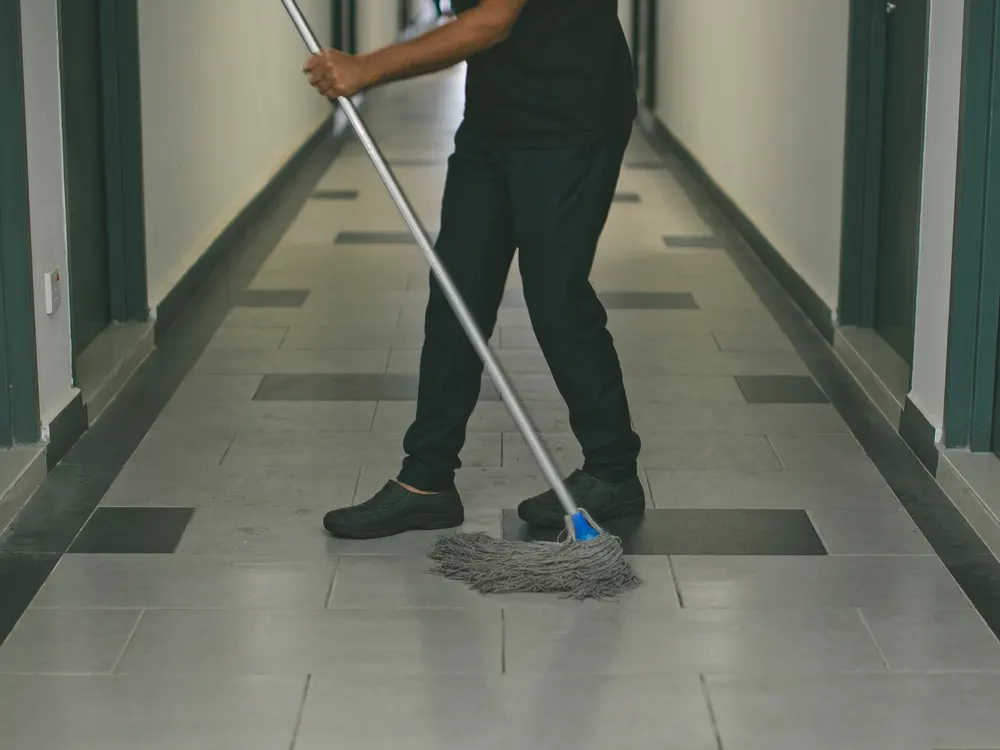 Profesional de limpieza fregando el suelo de un pasillo de acceso a viviendas