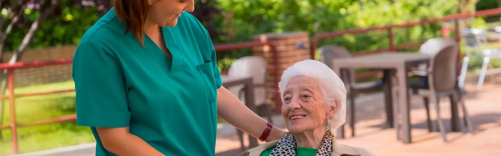 Cuidadora y mujer mayor cogidas de la mano en el jardín, las dos sonriendo